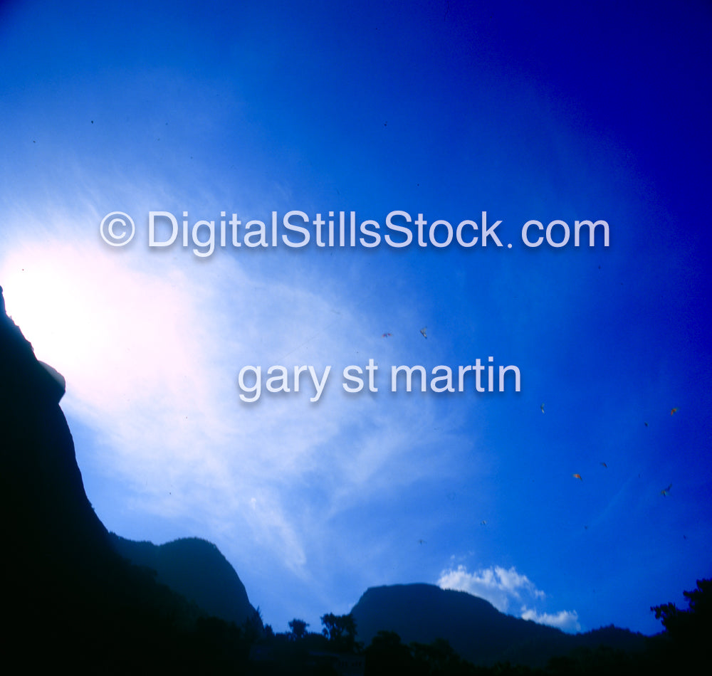 Silhouette of mountains against a bright blue sky with sun rays