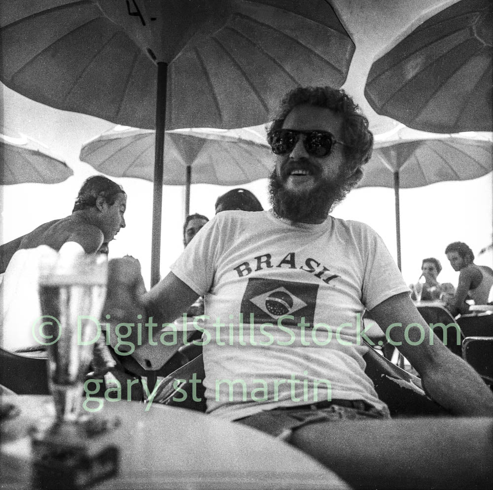 Man wearing a 'Brasil' t-shirt under umbrellas with people in the background