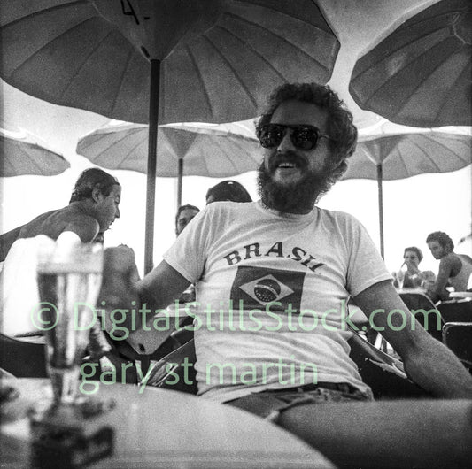 Man wearing a 'Brasil' t-shirt under umbrellas with people in the background