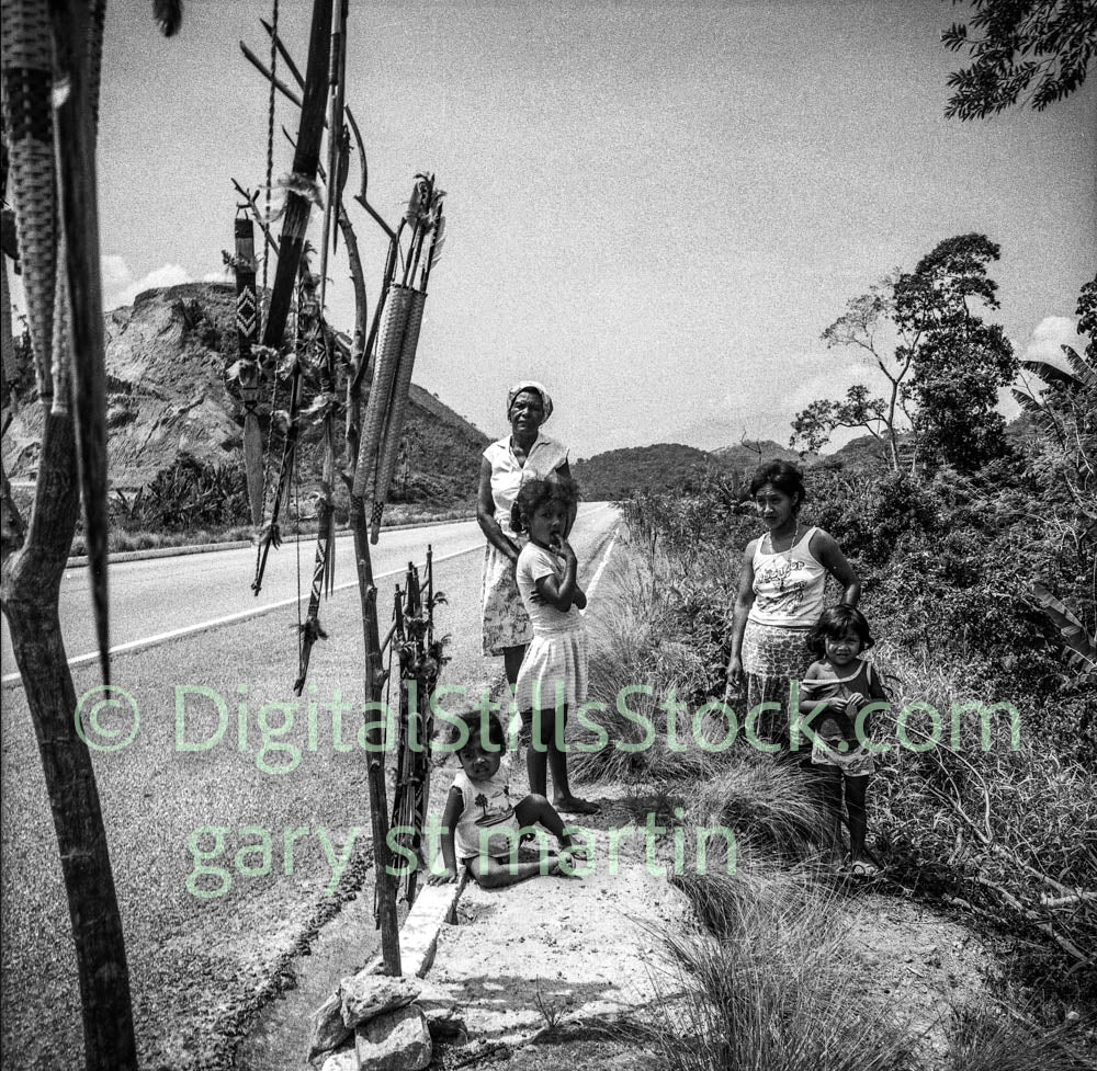 Black and white photograph of a family by a road with decorative items.