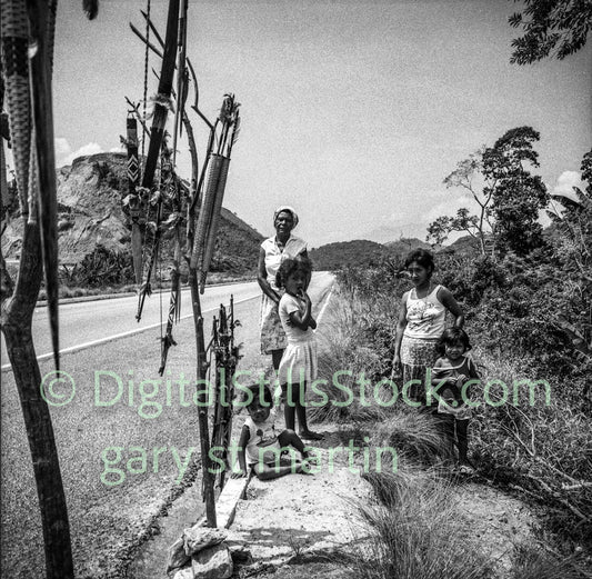 Black and white photograph of a family by a road with decorative items.