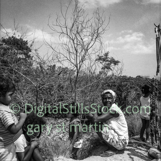 Black and white photograph of a woman and children outdoors with trees and sky in the background.