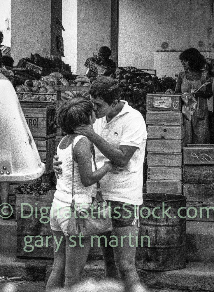 Black and white photo of a couple embracing in an outdoor market setting.