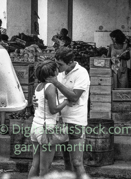 Black and white photo of a couple embracing in an outdoor market setting.