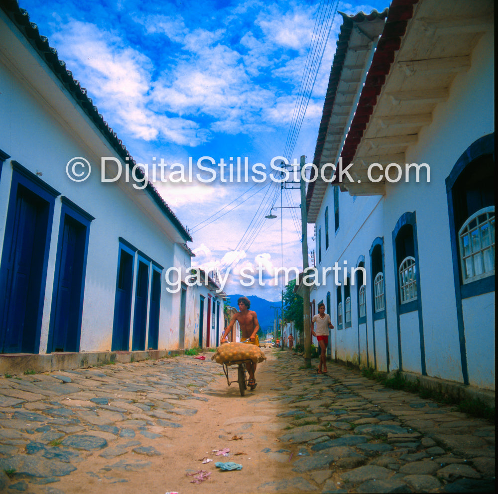Two people walking down a cobblestone street with white buildings and blue doors.